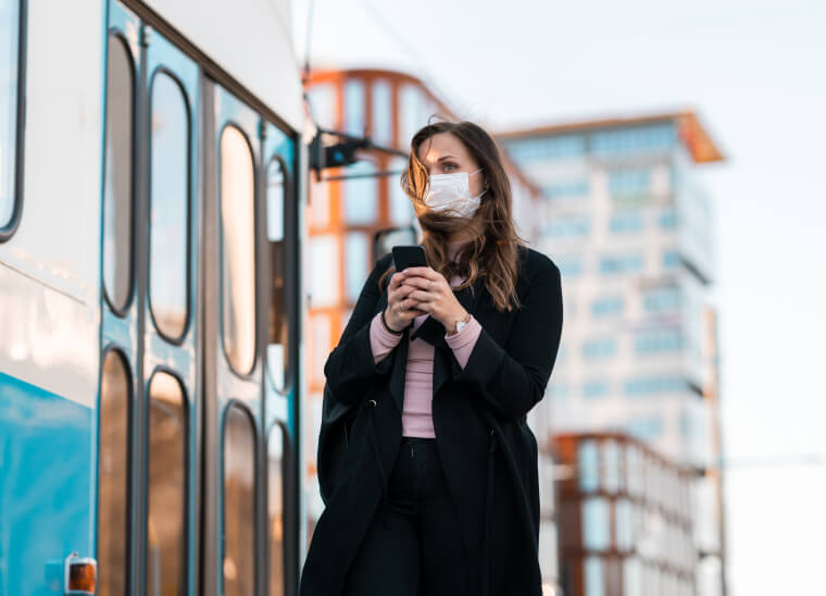 Woman outside wearing a mask and holding her phone.